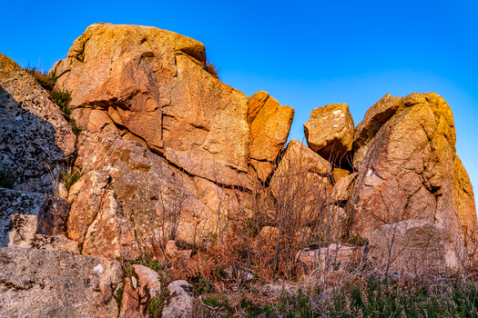 View of Kincasslagh Mass Rock featuring large weathered granite formations illuminated by golden sunlight under a clear blue sky in Kincasslagh County Donegal Ireland. View of Kincasslagh Mass Rock featuring large weathered granite formations illuminated by golden sunlight under a clear blue sky in Kincasslagh County Donegal Ireland.
