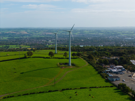 Aerial view of two wind turbines standing in a lush green field with grazing cattle and a distant town in the background in Lisburn Northern Ireland United Kingdom. Aerial view of two wind turbines standing in a lush green field with grazing cattle and a distant town in the background in Lisburn Northern Ireland United Kingdom.