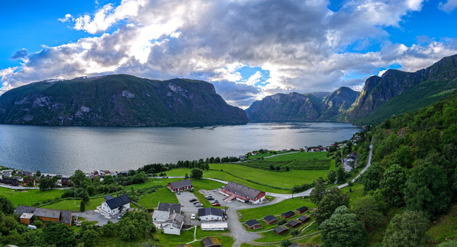 Aerial view of Flam village nestled along the Aurlandsfjord surrounded by lush green fields traditional buildings and steep mountains under a dramatic cloudy sky in Flam Vestland Norway. Aerial view of Flam village nestled along the Aurlandsfjord surrounded by lush green fields traditional buildings and steep mountains under a dramatic cloudy sky in Flam Vestland Norway.