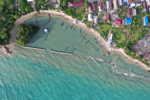 Aerial view of Pulau Maginti featuring traditional wooden boats anchored in turquoise waters near a coastal village with houses along the shore in Maginti South East Sulawesi Indonesia.