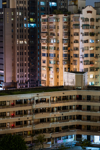 View of residential apartment buildings with illuminated windows and a multi story building with a green roof in the foreground in Sanchong District New Taipei City Taiwan. View of residential apartment buildings with illuminated windows and a multi story building with a green roof in the foreground in Sanchong District New Taipei City Taiwan.