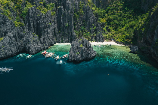 Aerial view of limestone cliffs surrounding a secluded beach with turquoise water and traditional outrigger boats anchored in El Nido Mimaropa Philippines. Aerial view of limestone cliffs surrounding a secluded beach with turquoise water and traditional outrigger boats anchored in El Nido Mimaropa Philippines.