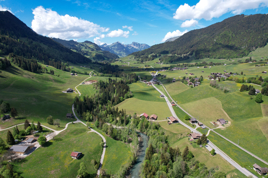 Aerial view of the lush green valley with traditional chalets a winding river and forested mountains under a blue sky in Rougemont Vaud Switzerland. Aerial view of the lush green valley with traditional chalets a winding river and forested mountains under a blue sky in Rougemont Vaud Switzerland.