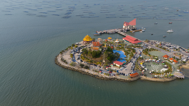 Aerial view of Koh Loi temple complex with its golden pagoda surrounding park parking areas and a pier extending into the sea in Si Racha Chon Buri Thailand. Aerial view of Koh Loi temple complex with its golden pagoda surrounding park parking areas and a pier extending into the sea in Si Racha Chon Buri Thailand.