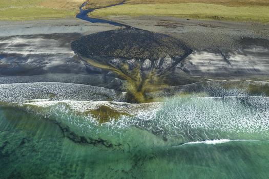 Aerial view of the dark volcanic sands and turquoise waves at Talisker Bay Beach with a river delta flowing into the sea Isle of Skye Scotland United Kingdom. Aerial view of the dark volcanic sands and turquoise waves at Talisker Bay Beach with a river delta flowing into the sea Isle of Skye Scotland United Kingdom.