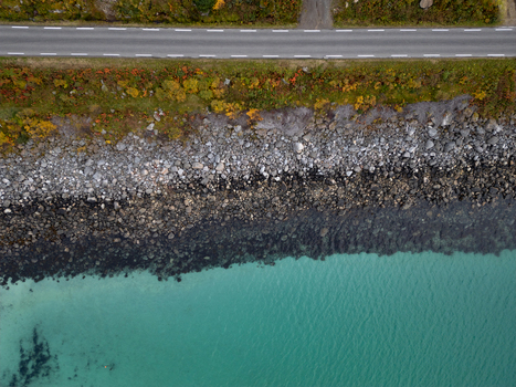 Aerial view of the coastal road at Rorvikstranda with a rocky shoreline and turquoise water surrounded by autumn vegetation in Henningsvaer Nordland Norway.