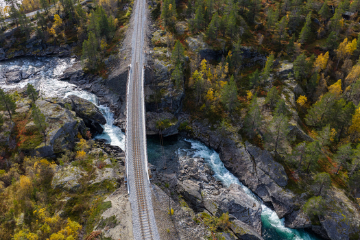 Aerial view of a railway bridge crossing a rushing river surrounded by rocky terrain and autumn forests in Bjorli Innlandet Norway. Aerial view of a railway bridge crossing a rushing river surrounded by rocky terrain and autumn forests in Bjorli Innlandet Norway.