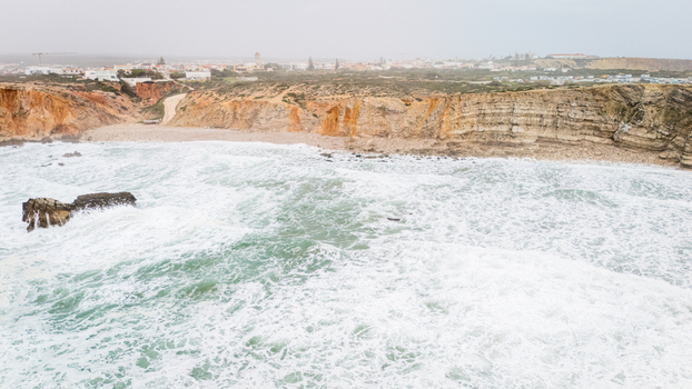 Aerial view of the rugged cliffs and crashing white waves along the coastline with the town in the distance Sagres Faro Portugal. Aerial view of the rugged cliffs and crashing white waves along the coastline with the town in the distance Sagres Faro Portugal.