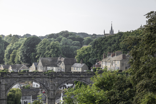 View of the historic Knaresborough Viaduct with its stone arches set against a backdrop of lush green trees and traditional stone buildings in Knaresborough England United Kingdom.