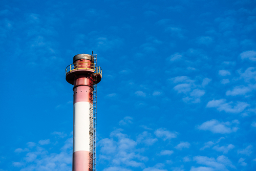 View of a tall red and white industrial smokestack with a metal ladder against a bright blue sky in Poland.