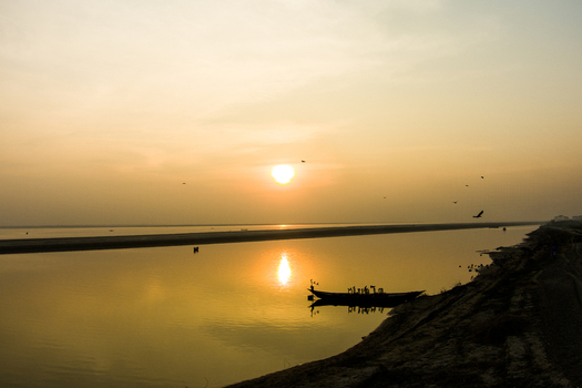 Aerial view of a small boat on the calm Padma River during a golden sunset with birds flying in the sky in Rajshahi Rajshahi Division Bangladesh.