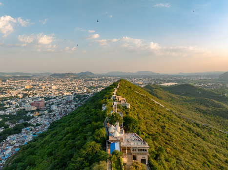 Aerial view of the Karni Mata Temple on a lush green hill overlooking the sprawling cityscape with white buildings and distant mountains under a clear sky in Udaipur Rajasthan India.