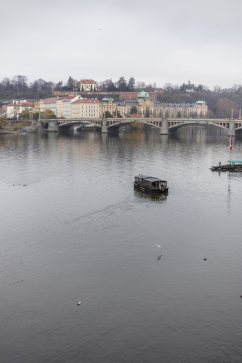 View of a tourist boat cruising on the Vltava River with the Manes Bridge and the Straka Academy under an overcast sky in Prague Prague Czechia. View of a tourist boat cruising on the Vltava River with the Manes Bridge and the Straka Academy under an overcast sky in Prague Prague Czechia.
