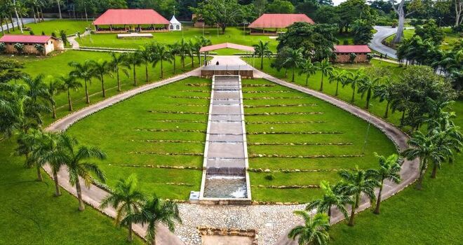 Aerial view of a landscaped park with a central cascading water feature lush green lawns and rows of palm trees in Ghana. Aerial view of a landscaped park with a central cascading water feature lush green lawns and rows of palm trees in Ghana.