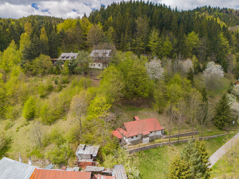Aerial view of traditional houses nestled on a lush green hillside surrounded by dense forest and blooming spring trees in Spania Dolina Banska Bystrica Regio Slovakia.