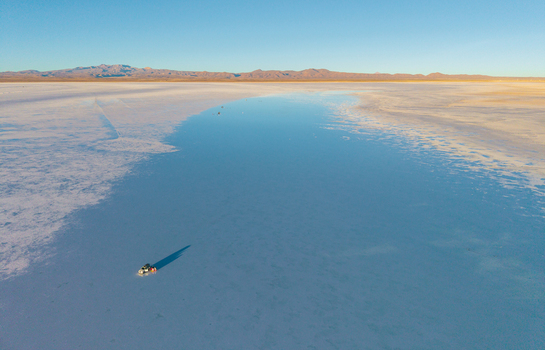 Aerial view of the Uyuni Salt Flat with a reflective salt crust and a vehicle casting a long shadow on the vast landscape in Uyuni Potosi Department Bolivia. Aerial view of the Uyuni Salt Flat with a reflective salt crust and a vehicle casting a long shadow on the vast landscape in Uyuni Potosi Department Bolivia.