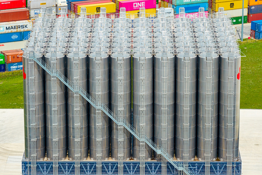 Poland 25 July 2026 Aerial view of a large industrial silo structure with metallic cylindrical tanks metal staircases and colorful shipping containers in the background.