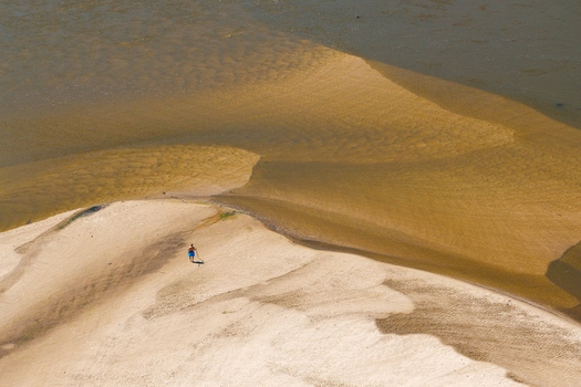 Aerial view of a riverbed with low water levels and exposed sandbanks with a person walking on the sand in Poland.