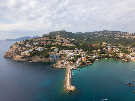 Aerial view of Port d Andratx featuring a long breakwater with a lighthouse turquoise waters and villas on the green hillsides in Port d Andratx Balearic Islands Spain. Aerial view of Port d Andratx featuring a long breakwater with a lighthouse turquoise waters and villas on the green hillsides in Port d Andratx Balearic Islands Spain.
