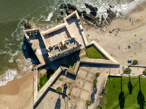 Aerial view of Forte de Sao Bruno a historic star shaped fortress situated on the coast with sandy beaches rocky shoreline and palm trees in Caxias Lisbon Portugal.
