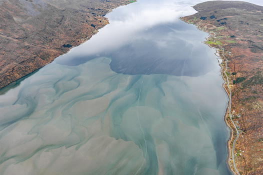 Aerial view of the dramatic fjord landscape with intricate tidal patterns in the shallow waters surrounded by rugged mountains and coastal roads in Senja Troms Norway.