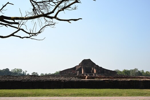 View of the ancient brick ruins of Sompur Mahavihara set against a clear sky with green lawns and tree branches in the foreground in Naogaon District Rajshahi Division Bangladesh. View of the ancient brick ruins of Sompur Mahavihara set against a clear sky with green lawns and tree branches in the foreground in Naogaon District Rajshahi Division Bangladesh.