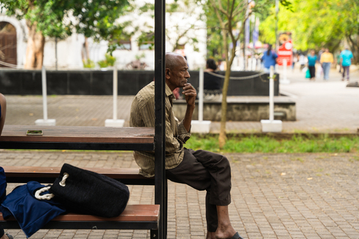 Sri Lanka 20 February 2026 View of an elderly man sitting on a wooden bench in a public park with people walking in the background.