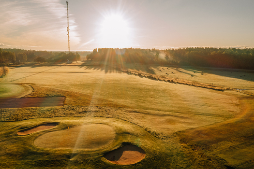 Aerial view of a golf course at golden hour with green fairways sand bunkers and long tree shadows in Valmiera Valmiera Latvija.