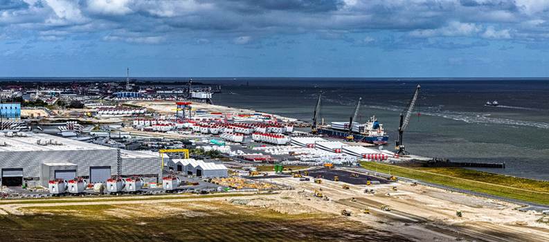 Aerial view of the Siemens Gamesa Renewable Energy facility in Cuxhaven with wind turbine blades nacelles cranes and a cargo ship at the port in Cuxhaven Niedersachsen Germany.
