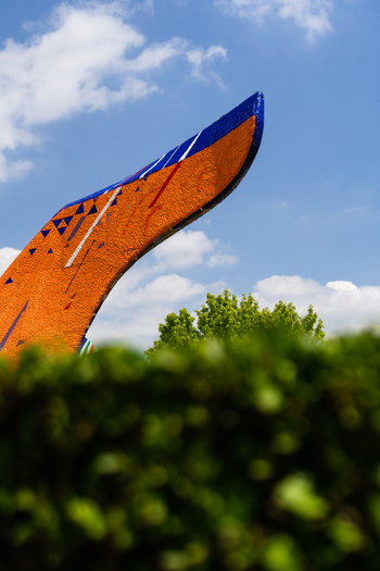 Bratislava Slovakia 09 May 2026 View of an orange and blue abstract sculpture rising above green bushes against a bright blue sky with scattered clouds.