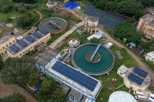 Aerial view of a water treatment plant with circular sedimentation tanks and rooftop solar panels on industrial buildings Karad Maharashtra India.