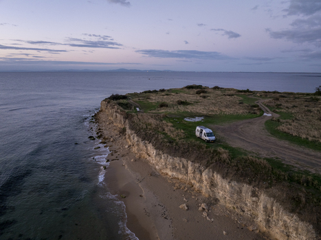 Aerial view of a camper van parked on a grassy cliff edge overlooking the sea at twilight with soft evening light and calm water Nessebar Burgas Bulgaria. Aerial view of a camper van parked on a grassy cliff edge overlooking the sea at twilight with soft evening light and calm water Nessebar Burgas Bulgaria.