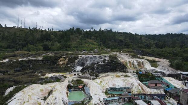 Aerial view of the Sipoholon hot springs with white limestone terraces geothermal pools and lush green hills in the background in Tarutung North Sumatra Indonesia. Aerial view of the Sipoholon hot springs with white limestone terraces geothermal pools and lush green hills in the background in Tarutung North Sumatra Indonesia.