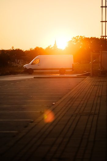 View of a white delivery van parked in a lot during golden hour with a church spire silhouette in the background in Sremska Mitrovica Vojvodina Serbia.