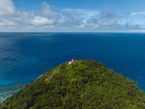 Aerial view of a green tree covered cape with bright blue waters surrounding it topped with a church Lifou New Caledonia. Aerial view of a green tree covered cape with bright blue waters surrounding it topped with a church Lifou New Caledonia.