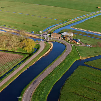 Aerial view of the historic Wipbrug drawbridge and a traditional house situated along a winding canal surrounded by lush green fields Spanbroek North Holland Netherlands.