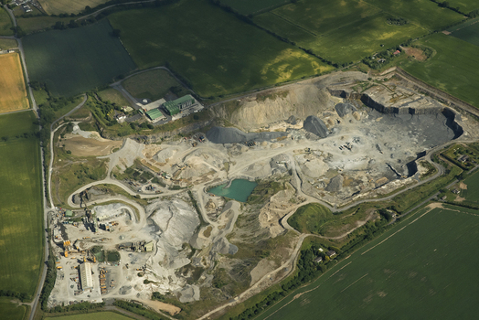 Aerial view of Roadstone Kilmacow quarry with industrial machinery gravel piles and a small pond surrounded by green fields in Kilmacow County Kilkenny Ireland.