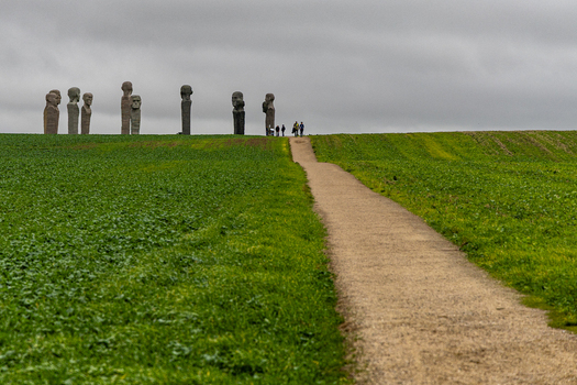 View of Dodekalitten stone sculptures standing on a grassy hill with a dirt path and people walking under an overcast sky in Kragenaes Lolland Denmark. View of Dodekalitten stone sculptures standing on a grassy hill with a dirt path and people walking under an overcast sky in Kragenaes Lolland Denmark.