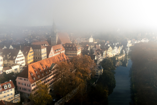 Aerial view of the historic old town with colorful half timbered houses along the Neckar river and the Stiftskirche spire emerging from thick morning fog in Tubingen Baden Wurttemberg Germany. Aerial view of the historic old town with colorful half timbered houses along the Neckar river and the Stiftskirche spire emerging from thick morning fog in Tubingen Baden Wurttemberg Germany.
