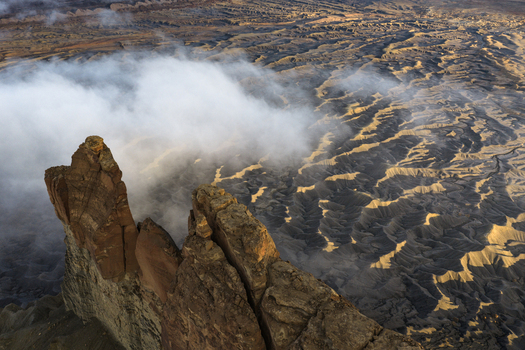 Aerial view of rugged desert rock formations and a tall sandstone pinnacle partially covered by low lying clouds in the badlands of Hanksville Utah United States.