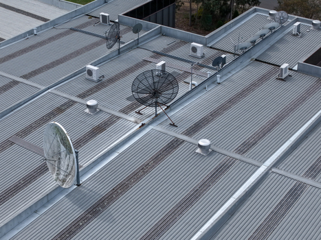 Melbourne VIC Australia 25 September 2026 Aerial view of a corrugated metal industrial roof featuring multiple satellite dishes HVAC units and ventilation vents.
