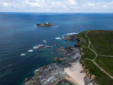 Aerial view of Godrevy Lighthouse on a rocky island near the sandy shores of Godrevy Beach and green coastal cliffs under a cloudy sky in Gwithian England United Kingdom. Aerial view of Godrevy Lighthouse on a rocky island near the sandy shores of Godrevy Beach and green coastal cliffs under a cloudy sky in Gwithian England United Kingdom.