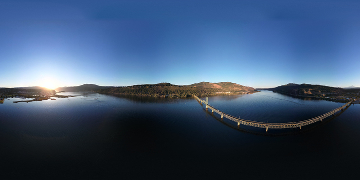 Aerial view of the Hood River White Salmon Bridge spanning the Columbia River at sunset with calm waters and rolling hills in the background in Hood River County Oregon United States. Aerial view of the Hood River White Salmon Bridge spanning the Columbia River at sunset with calm waters and rolling hills in the background in Hood River County Oregon United States.