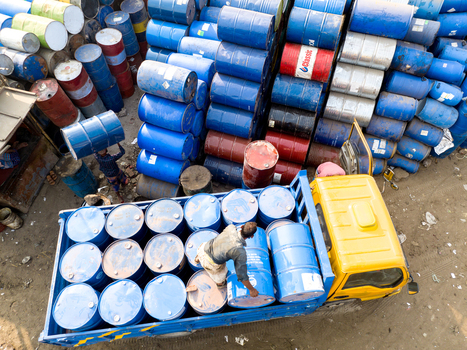 Aerial view of workers loading blue metal barrels onto a yellow truck next to large stacks of industrial drums in Dhaka Dhaka Division Bangladesh. Aerial view of workers loading blue metal barrels onto a yellow truck next to large stacks of industrial drums in Dhaka Dhaka Division Bangladesh.
