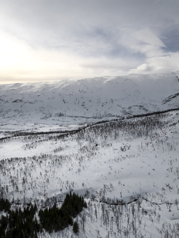 Aerial view of snow covered mountains and sparse evergreen forests under a cloudy winter sky in the arctic wilderness Kvaloya Troms Norway. Aerial view of snow covered mountains and sparse evergreen forests under a cloudy winter sky in the arctic wilderness Kvaloya Troms Norway.