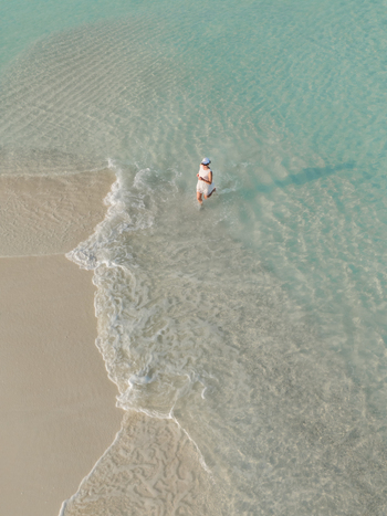 Aerial view of a person enjoying the crystal clear turquoise water meeting the soft sandy beach in Kan island Dhidhdhoo Thiladhunmathi Atoll Maldives.