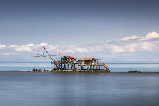 View of traditional fishing huts on stilts over the calm blue sea under a soft cloudy sky in Marina di Pisa Tuscany Italy.