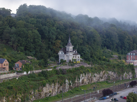 Aerial view of a historic villa perched on a cliffside surrounded by lush green forest with railway tracks running below in Dinant Wallonia Belgium.