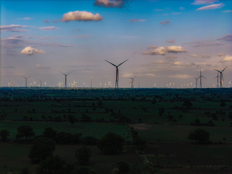 Aerial view of wind turbines standing in a rural landscape with green fields under a blue sky in Hampi Karnataka India.