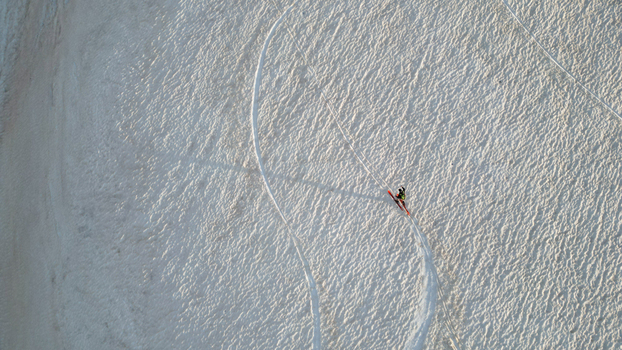 Aerial view of a lone skier crossing the snowy slopes of Le Colomby de Gex with curved tracks on the textured white surface in Echenevex Auvergne Rhone Alpes France. Aerial view of a lone skier crossing the snowy slopes of Le Colomby de Gex with curved tracks on the textured white surface in Echenevex Auvergne Rhone Alpes France.